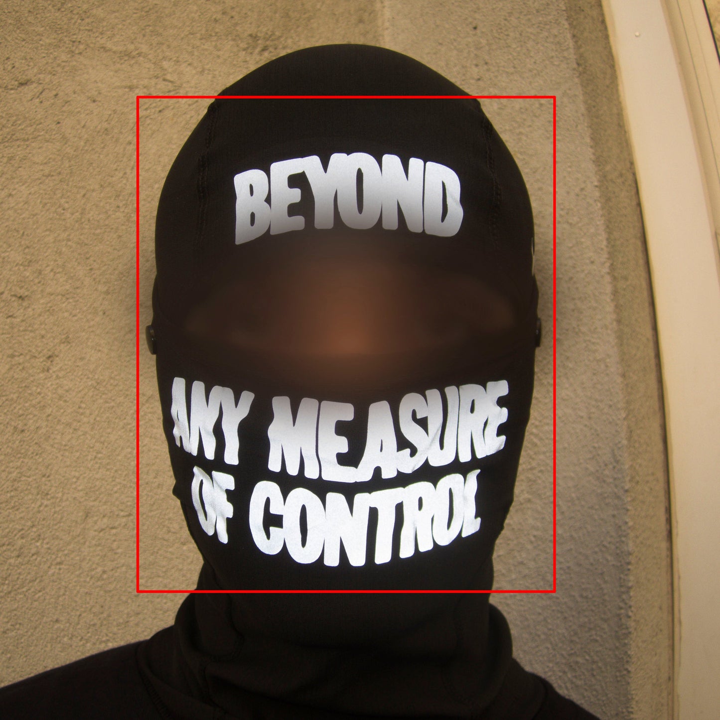 Person wearing a black balaclava with text 'BEYOND ANY MEASURE OF CONTROL' on a plain background